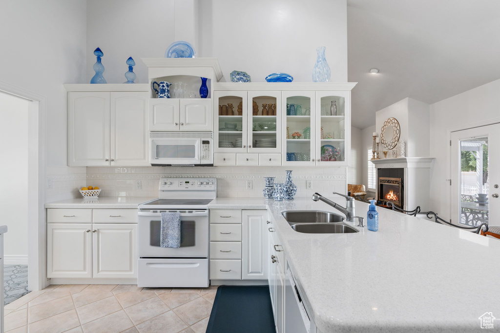 Kitchen with white appliances, light tile patterned floors, sink, decorative backsplash, and white cabinets