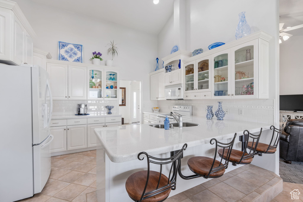 Kitchen with white appliances, kitchen peninsula, white cabinets, and a breakfast bar