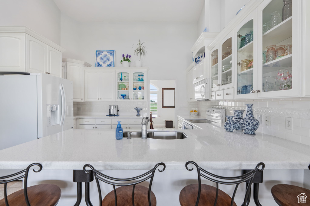 Kitchen with a breakfast bar, sink, white appliances, and white cabinetry