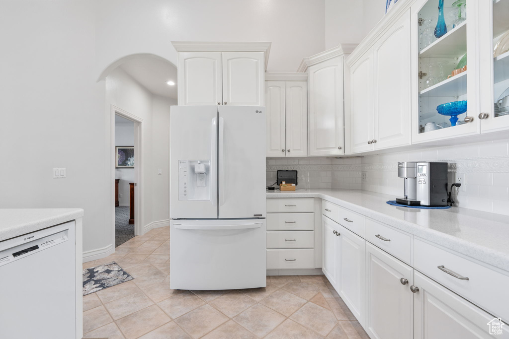 Kitchen with light tile patterned floors, white appliances, tasteful backsplash, and white cabinetry