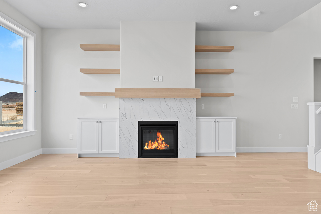 Unfurnished living room featuring light wood-style floors, a premium fireplace, baseboards, and recessed lighting