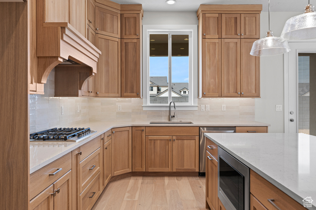 Kitchen with stainless steel appliances, a sink, light wood-style flooring, and light stone countertops