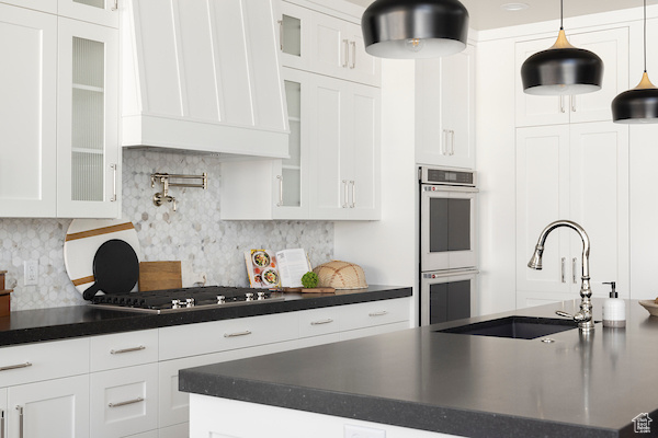 Kitchen with appliances with stainless steel finishes, white cabinetry, backsplash, and hanging light fixtures