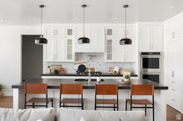 Kitchen featuring double oven, hanging light fixtures, a center island with sink, and a breakfast bar