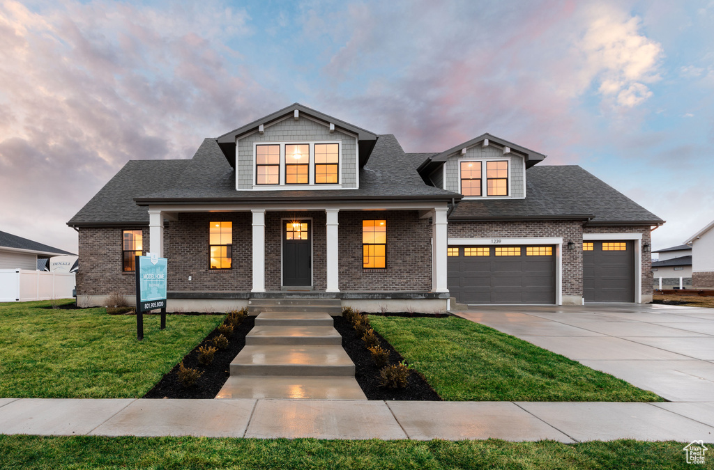 View of front of property featuring covered porch, a garage, and a front lawn