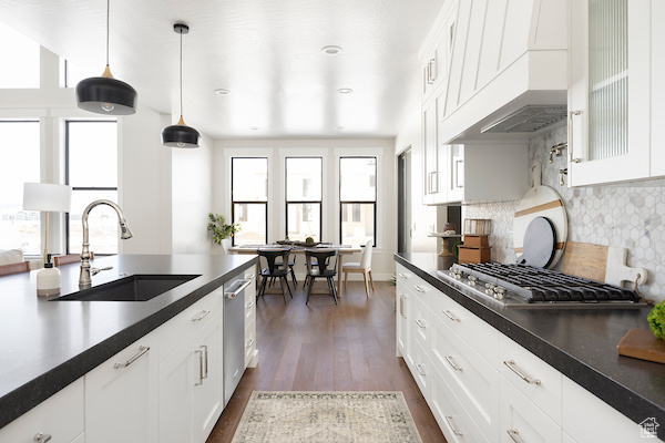 Kitchen featuring backsplash, hanging light fixtures, dark wood-type flooring, sink, and white cabinetry