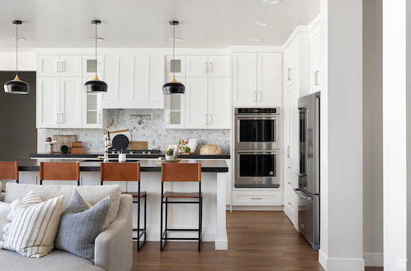 Kitchen featuring pendant lighting, appliances with stainless steel finishes, white cabinets, and a kitchen island with sink