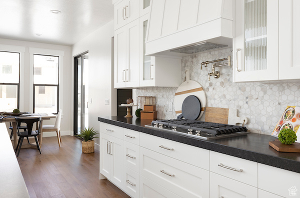 Kitchen featuring dark hardwood / wood-style flooring, stainless steel gas cooktop, backsplash, white cabinetry, and custom exhaust hood