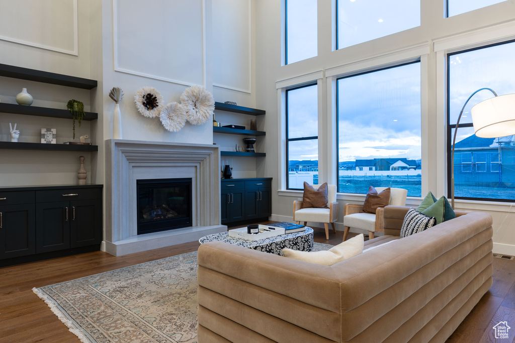 Living room featuring dark wood-type flooring, built in features, a water view, and a high ceiling