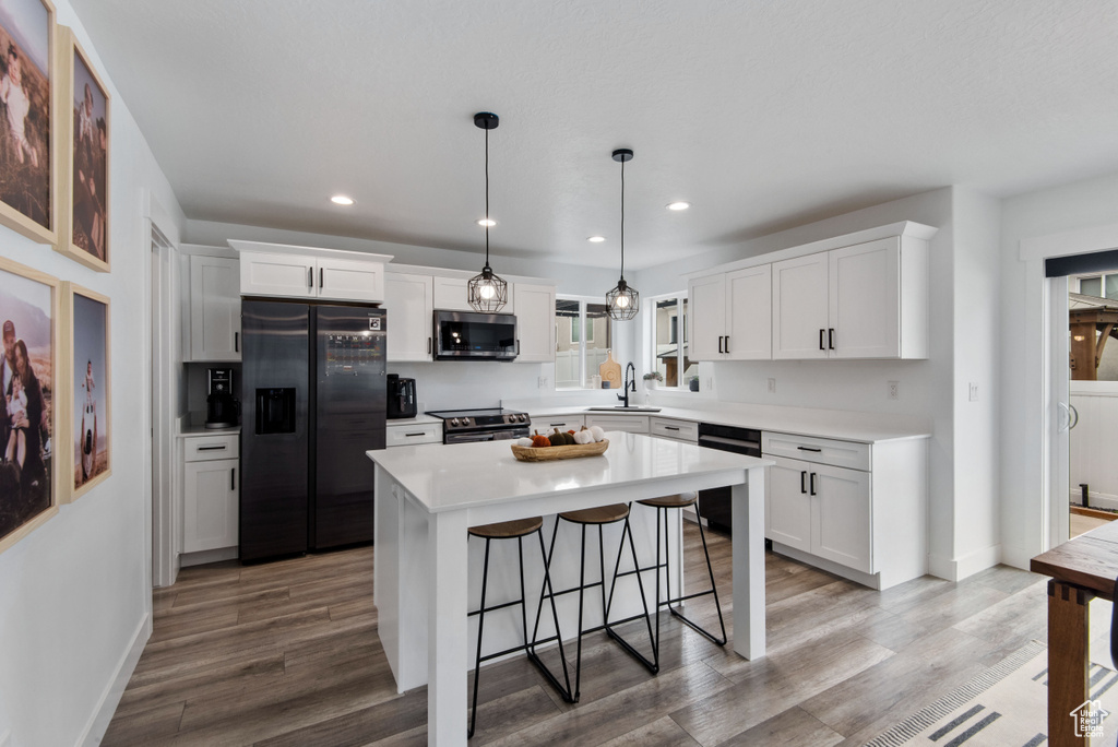 Kitchen featuring black appliances, sink, a center island, and white cabinetry