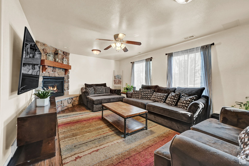 Living room featuring ceiling fan, a fireplace, wood-type flooring, and a textured ceiling