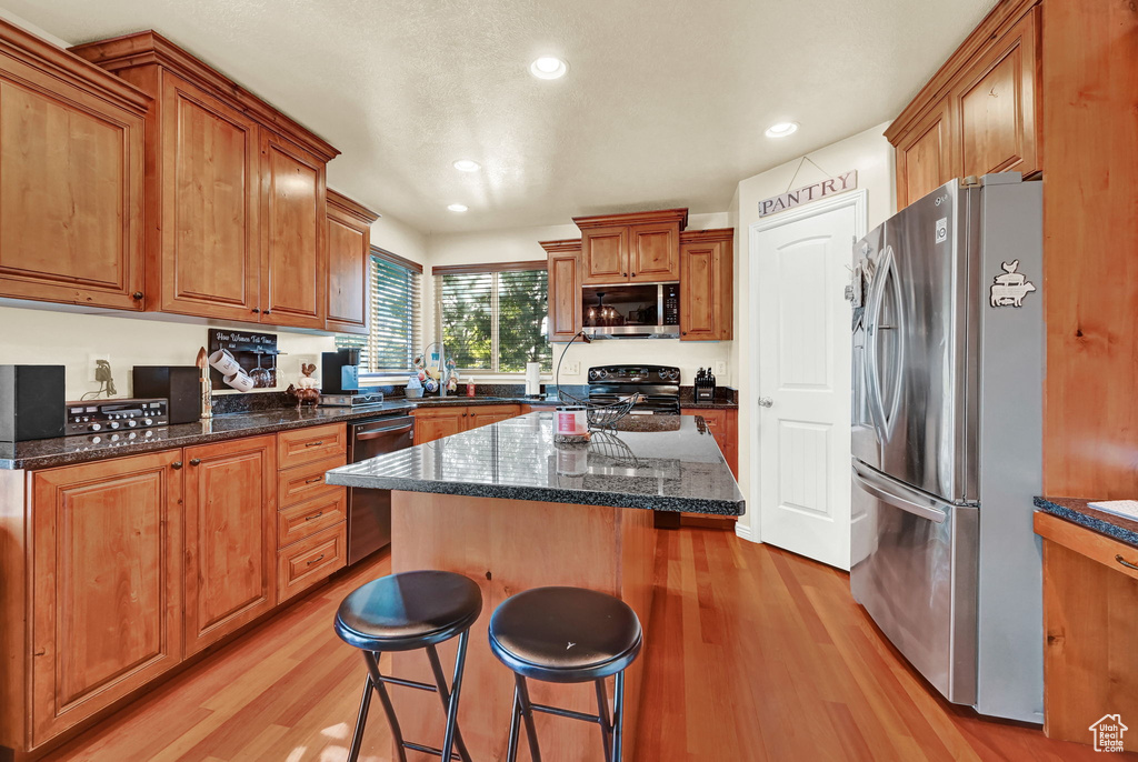 Kitchen with a kitchen island, a kitchen breakfast bar, light hardwood / wood-style floors, stainless steel appliances, and dark stone countertops