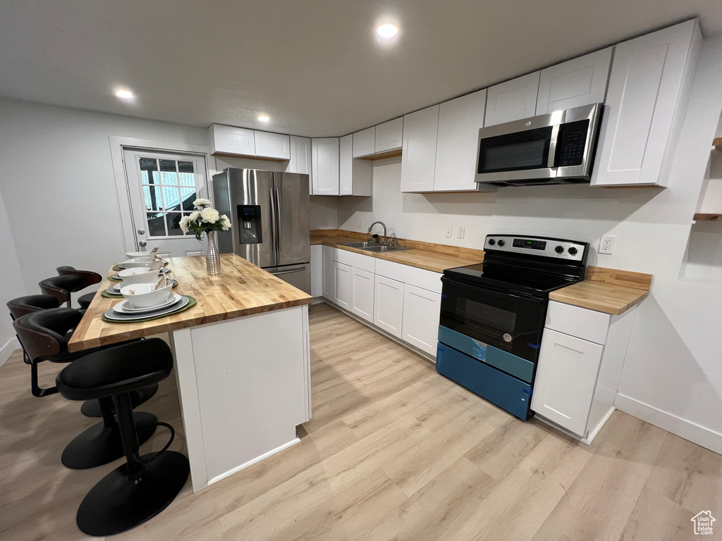 Kitchen featuring stainless steel appliances, sink, butcher block counters, and white cabinets