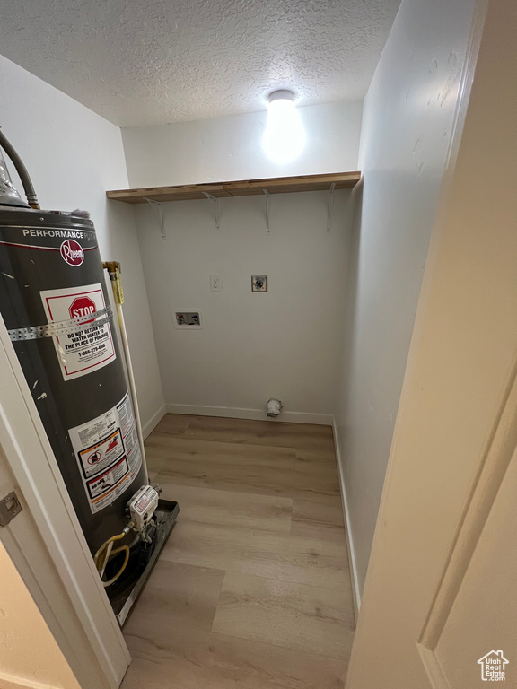 Laundry room featuring gas water heater, hookup for a washing machine, light hardwood / wood-style flooring, electric dryer hookup, and a textured ceiling