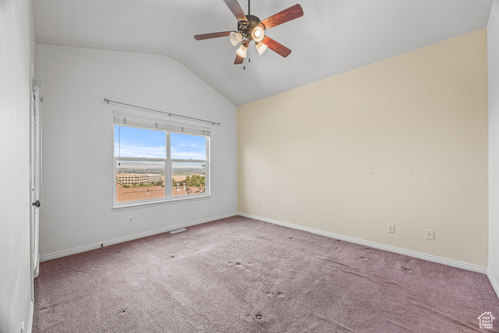 Empty room featuring vaulted ceiling, ceiling fan, and carpet flooring