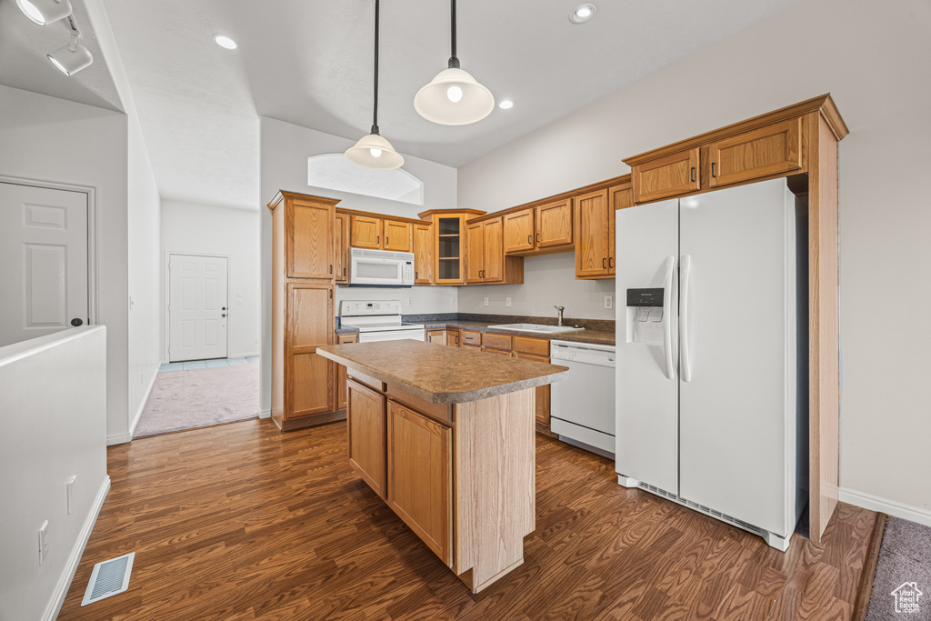 Kitchen featuring hanging light fixtures, white appliances, sink, dark wood-type flooring, and a kitchen island