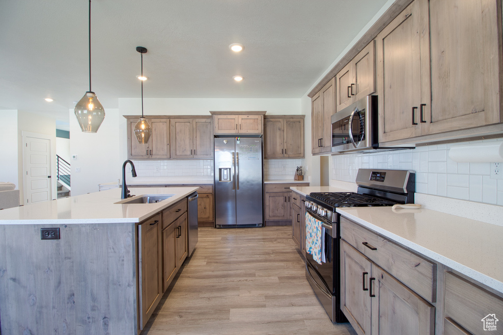 Kitchen with decorative light fixtures, a center island with sink, light hardwood / wood-style floors, stainless steel appliances, and sink