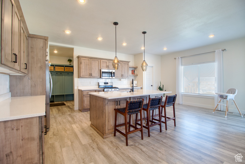 Kitchen featuring backsplash, light hardwood / wood-style flooring, decorative light fixtures, stainless steel appliances, and an island with sink