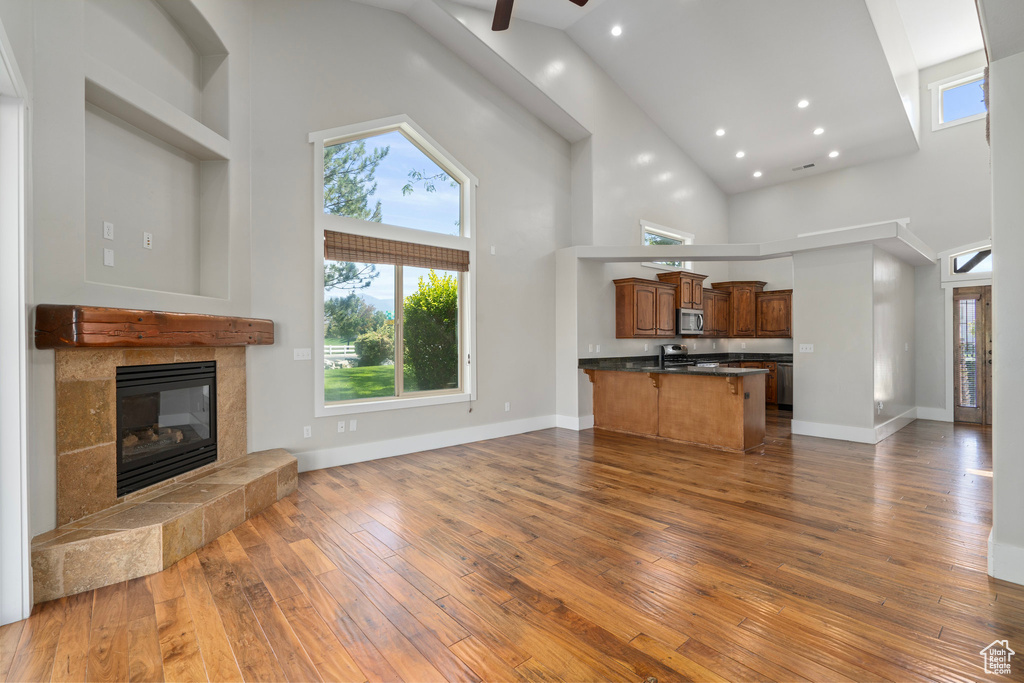 Unfurnished living room featuring dark wood-type flooring, high vaulted ceiling, a tile fireplace, and ceiling fan