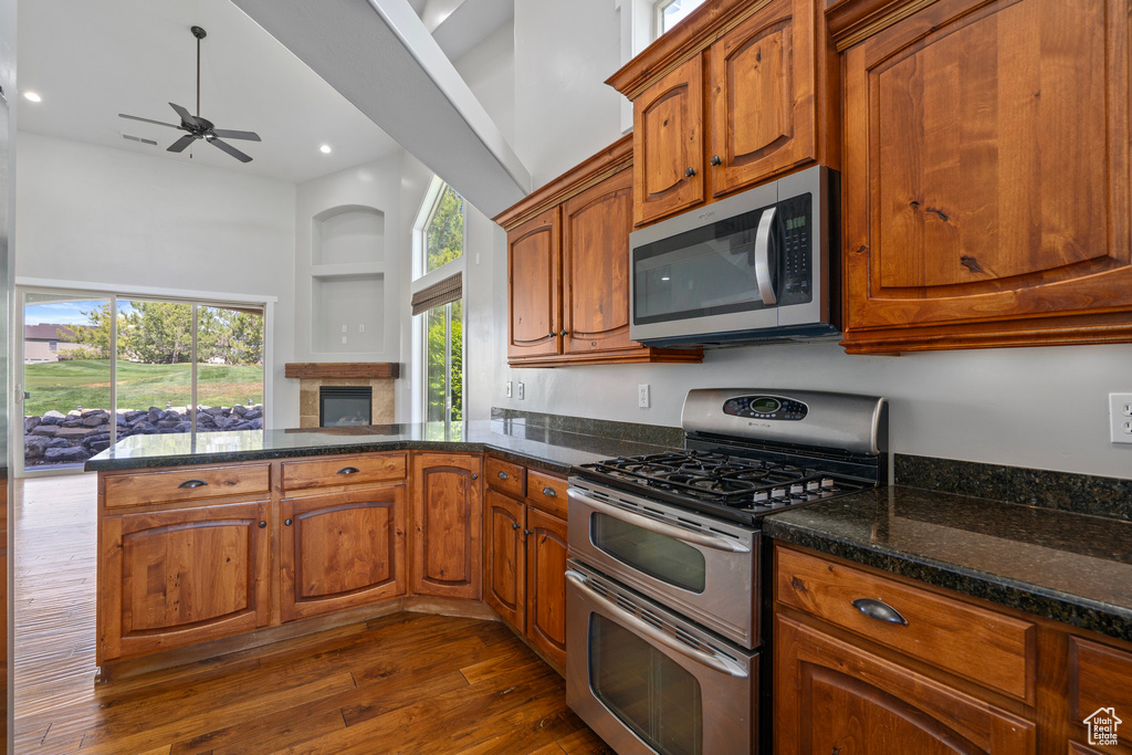 Kitchen featuring dark stone countertops, stainless steel appliances, dark hardwood / wood-style flooring, kitchen peninsula, and ceiling fan