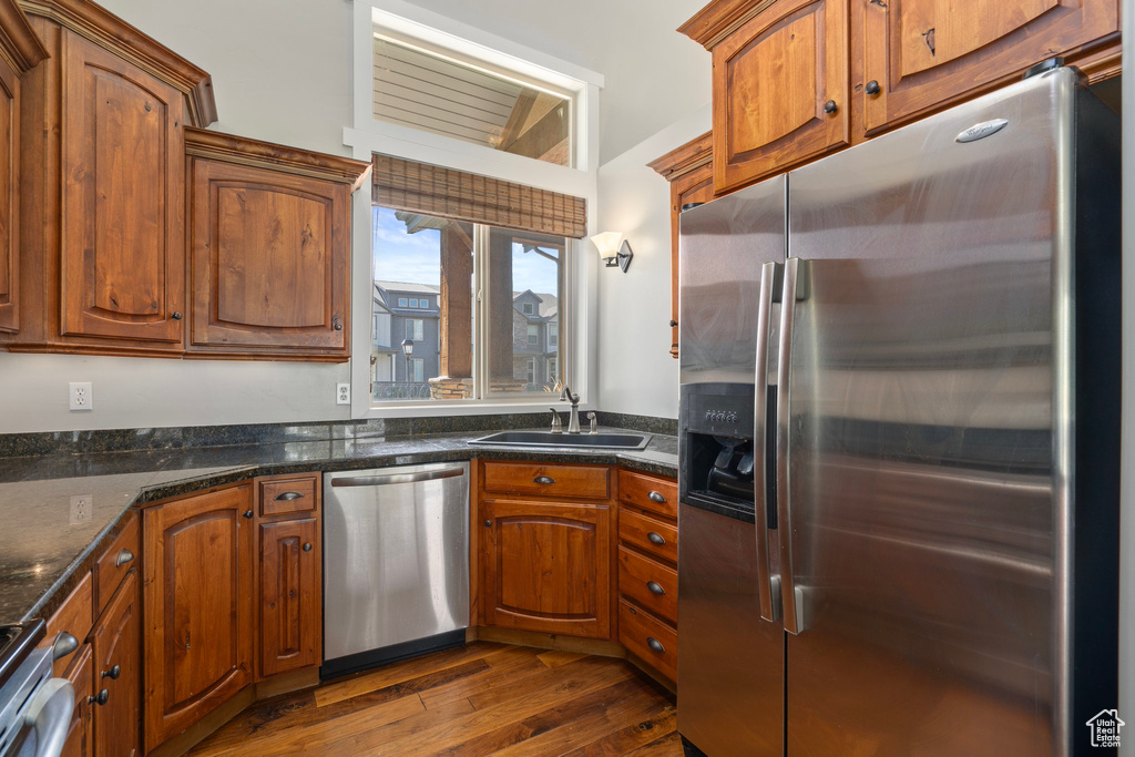 Kitchen with dark wood-type flooring, dark stone countertops, stainless steel appliances, and sink