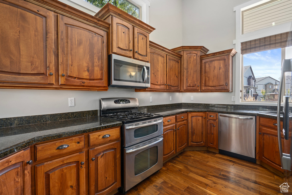 Kitchen featuring dark wood-type flooring, appliances with stainless steel finishes, and dark stone counters