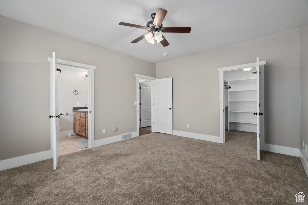 Unfurnished bedroom with ensuite bath, light carpet, a closet, a spacious closet, and ceiling fan