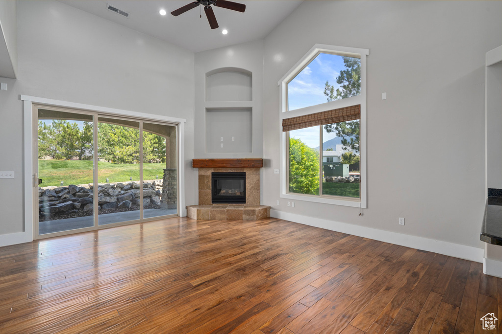 Unfurnished living room featuring hardwood / wood-style floors, built in features, a tile fireplace, ceiling fan, and a towering ceiling