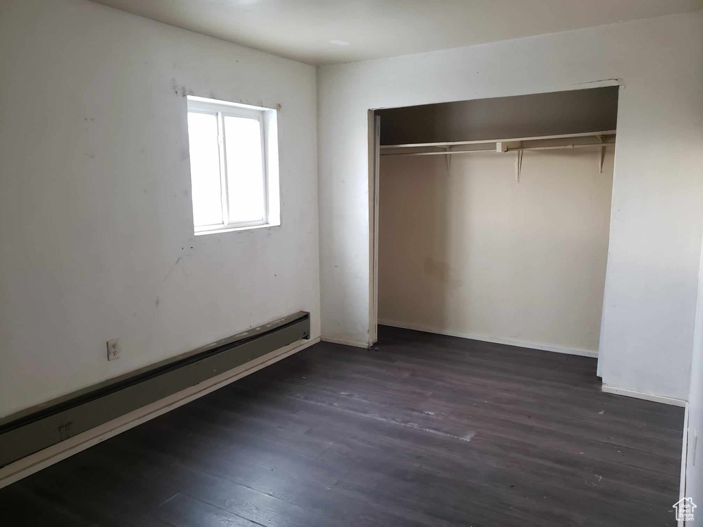 Unfurnished bedroom featuring a baseboard heating unit, dark hardwood / wood-style flooring, and a closet