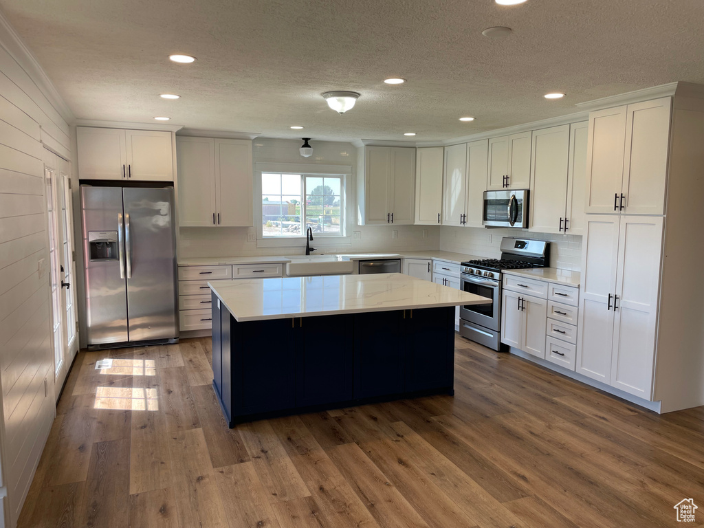 Kitchen with white cabinets, stainless steel appliances, wood-type flooring, and a kitchen island