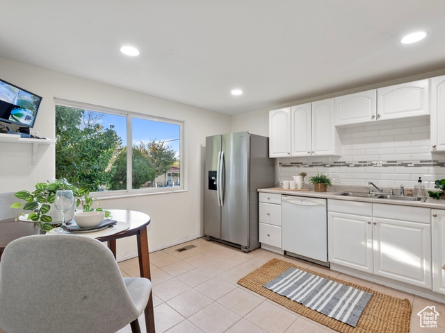 Kitchen with dishwasher, sink, white cabinets, decorative backsplash, and stainless steel fridge