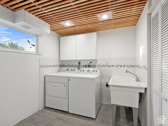 Clothes washing area with cabinets, tile walls, and washing machine and dryer