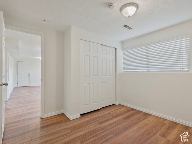 Unfurnished bedroom with a textured ceiling, light wood-type flooring, and a closet