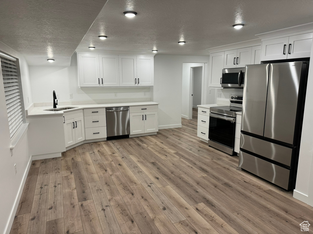 Kitchen featuring a textured ceiling, light hardwood / wood-style flooring, appliances with stainless steel finishes, sink, and white cabinets