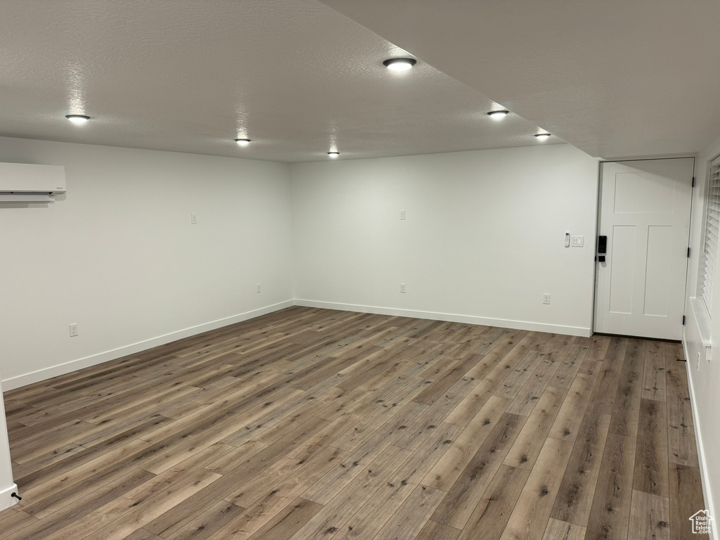 Basement with a textured ceiling, a wall unit AC, and dark hardwood / wood-style floors