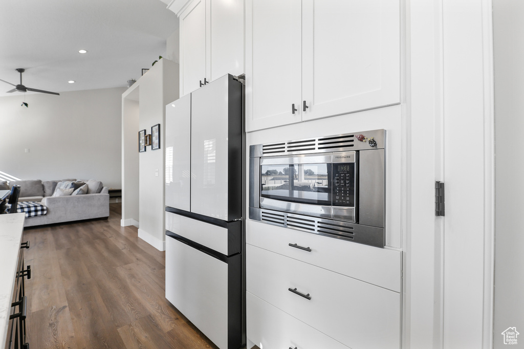 Kitchen featuring white refrigerator, ceiling fan, dark hardwood / wood-style floors, stainless steel microwave, and white cabinets