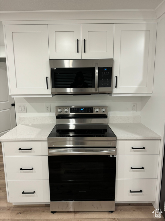 Kitchen with appliances with stainless steel finishes, white cabinetry, and light hardwood / wood-style flooring