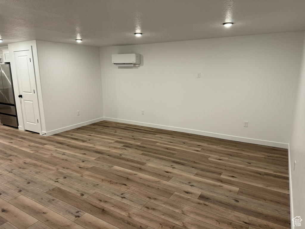 Basement with a wall unit AC, dark hardwood / wood-style flooring, stainless steel refrigerator, and a textured ceiling