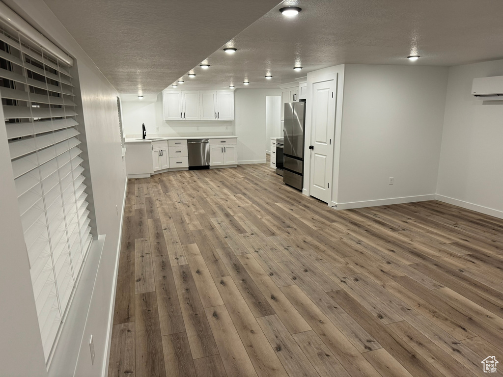 Unfurnished living room with light wood-type flooring, a textured ceiling, an AC wall unit, and sink