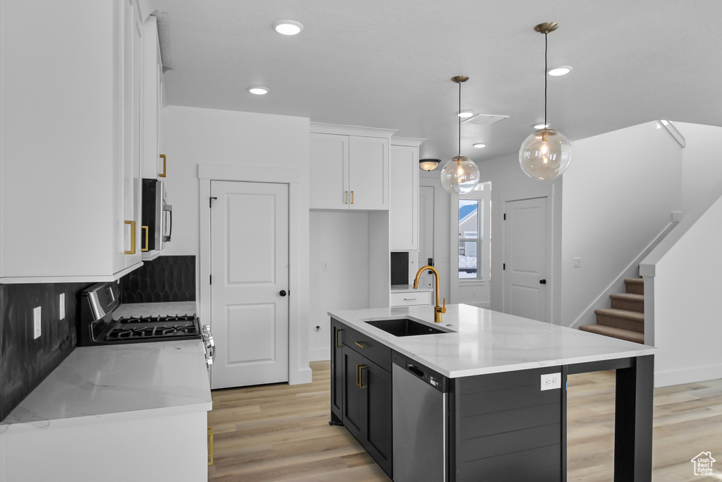 Kitchen with hanging light fixtures, stainless steel appliances, white cabinetry, sink, and an island with sink