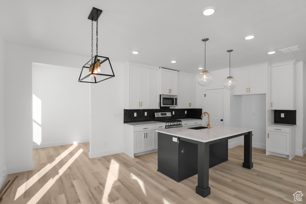 Kitchen with light hardwood / wood-style floors, a kitchen island with sink, stainless steel appliances, sink, and white cabinets