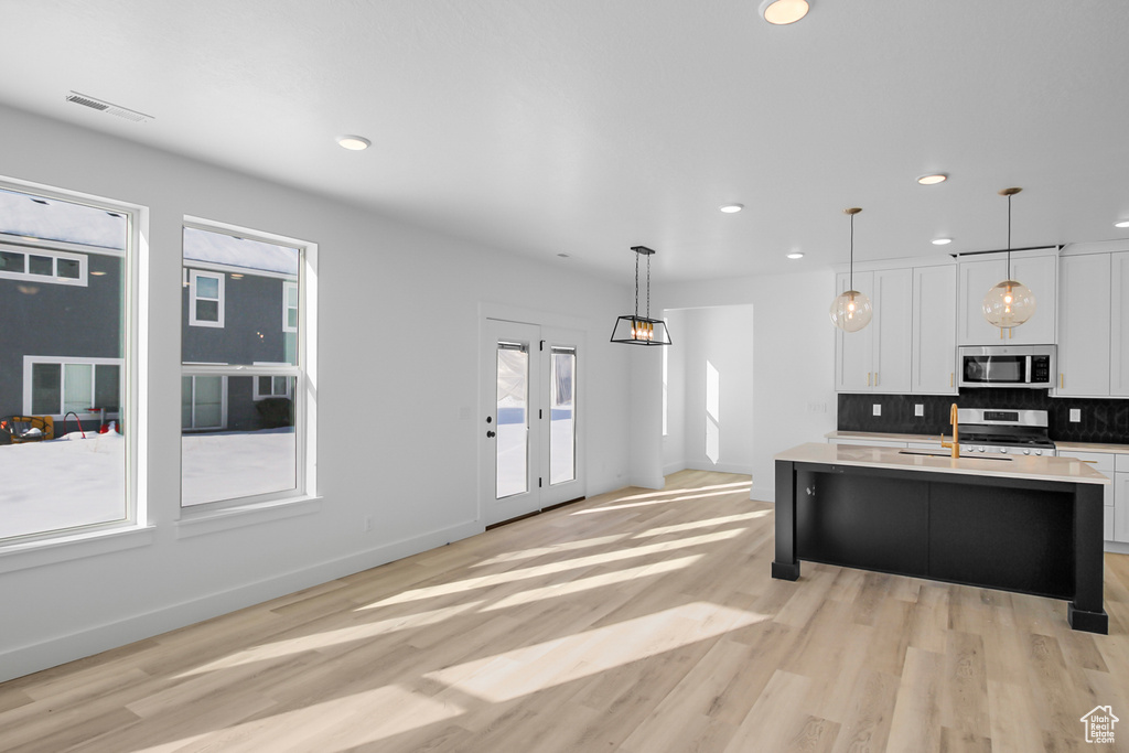 Kitchen featuring white cabinetry, hanging light fixtures, appliances with stainless steel finishes, a center island with sink, and light hardwood / wood-style floors