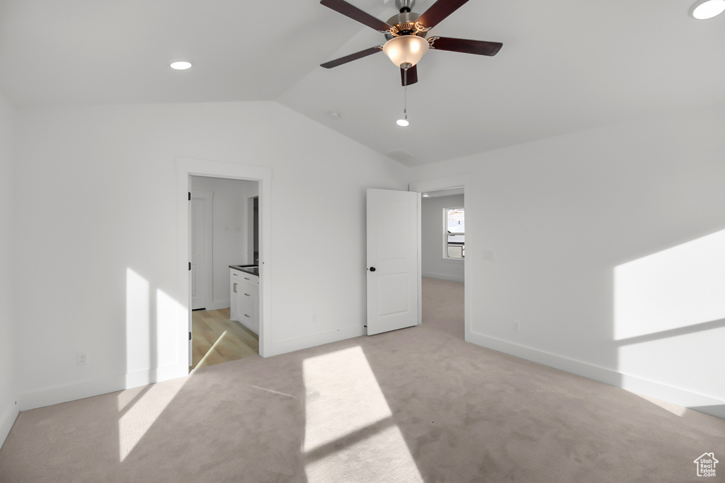 Unfurnished bedroom featuring vaulted ceiling, ceiling fan, ensuite bathroom, and light colored carpet