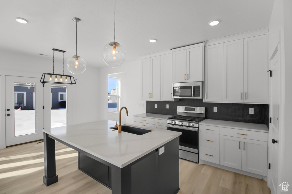 Kitchen with white cabinets, stainless steel appliances, a kitchen island with sink, and sink