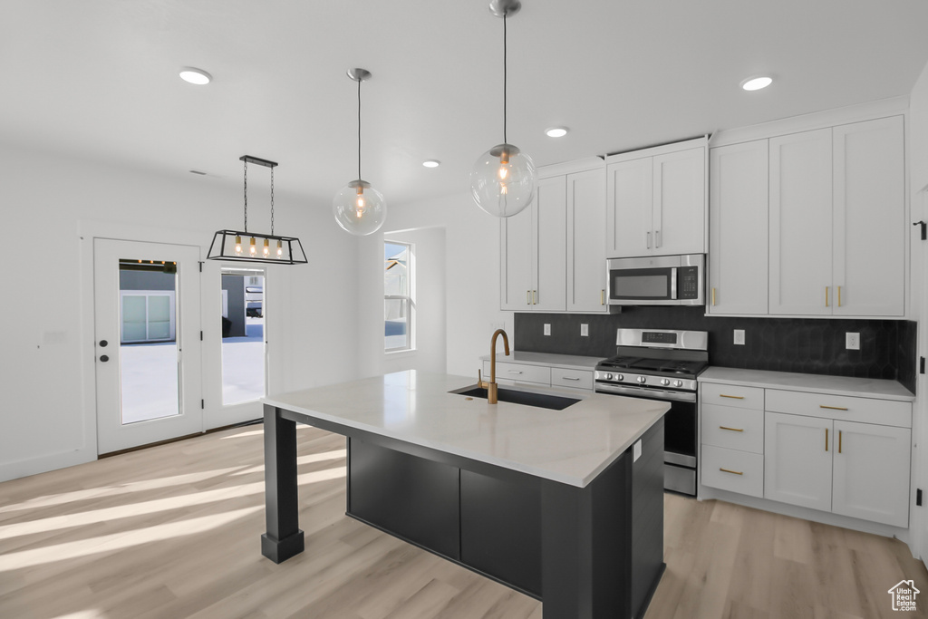 Kitchen featuring a center island with sink, appliances with stainless steel finishes, hanging light fixtures, sink, and white cabinets