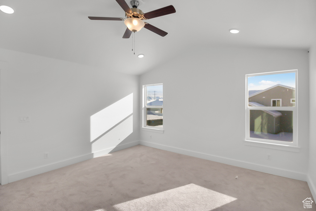 Spare room featuring vaulted ceiling, light colored carpet, a wealth of natural light, and ceiling fan