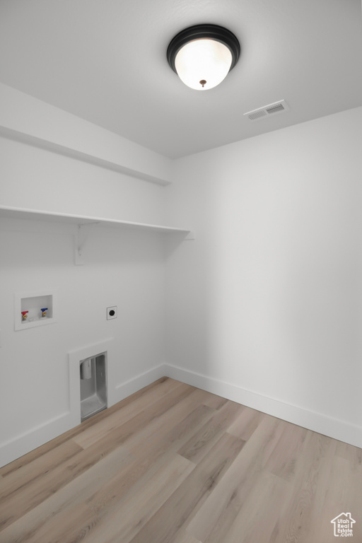 Clothes washing area with hookup for a washing machine, electric dryer hookup, and light wood-type flooring