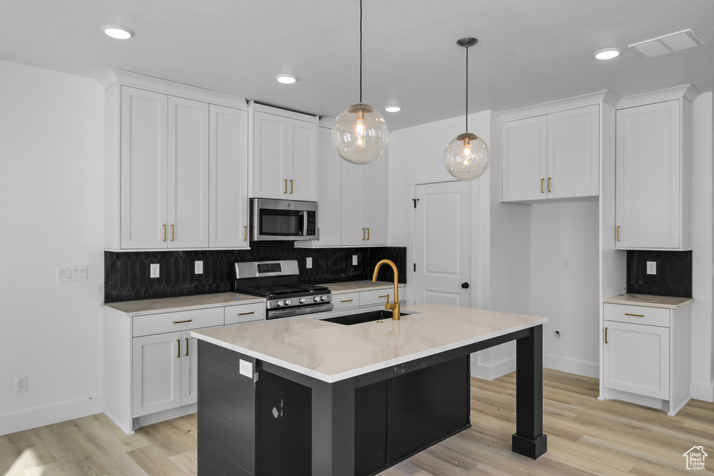 Kitchen with hanging light fixtures, appliances with stainless steel finishes, white cabinetry, sink, and a center island with sink