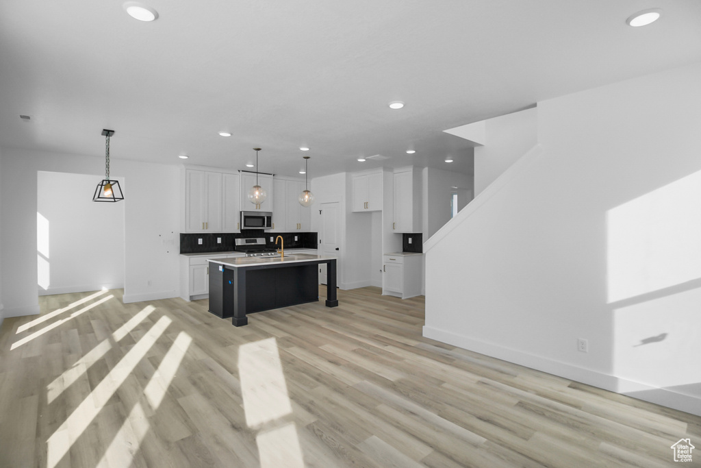 Kitchen with light hardwood / wood-style floors, pendant lighting, an island with sink, and white cabinetry