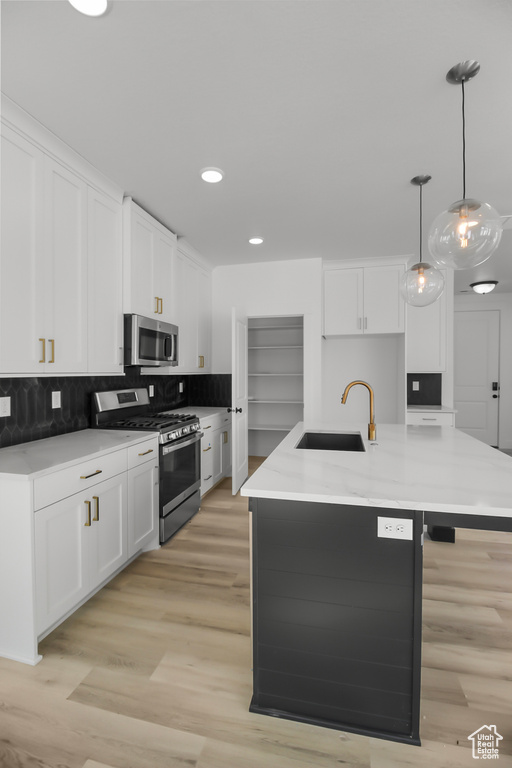 Kitchen featuring white cabinetry, sink, hanging light fixtures, appliances with stainless steel finishes, and a center island with sink